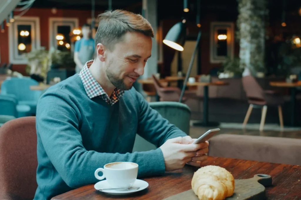 Customer scrolling his phone over coffee in a café, the kind of local audience behind UK Instagram ads cost benchmarks