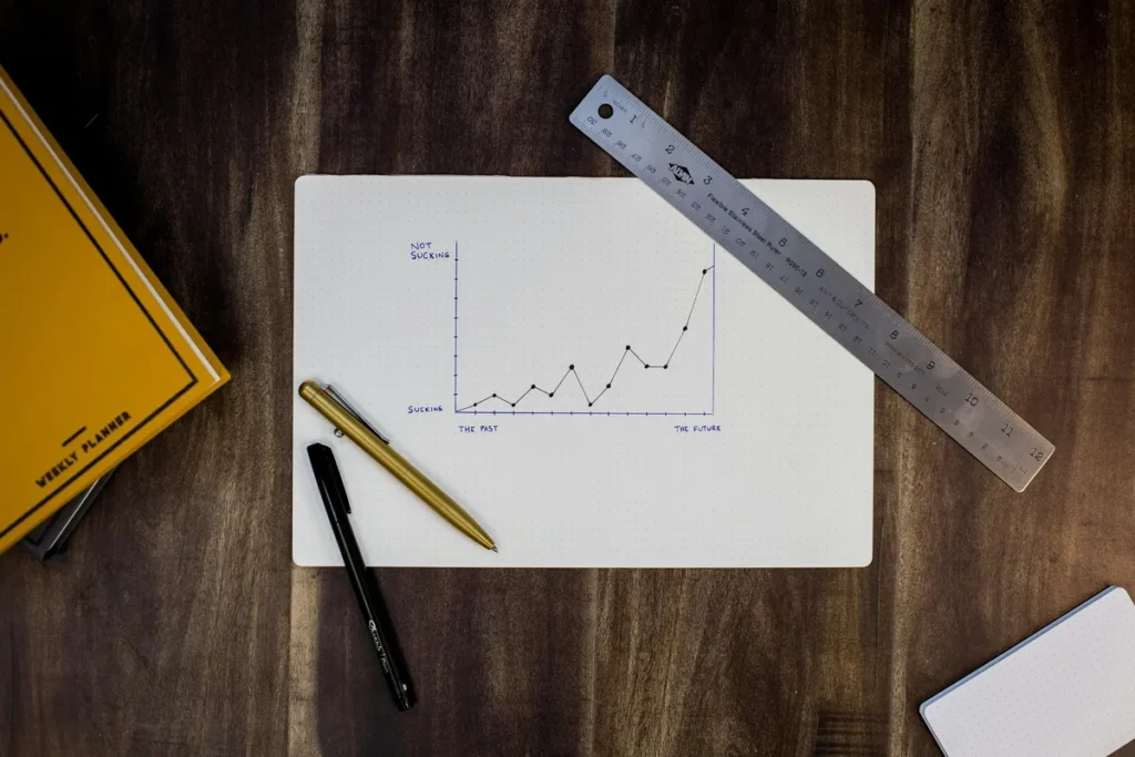 Hand-drawn line graph on paper with a ruler and pens, the kind of progress a monthly SEO report tracks